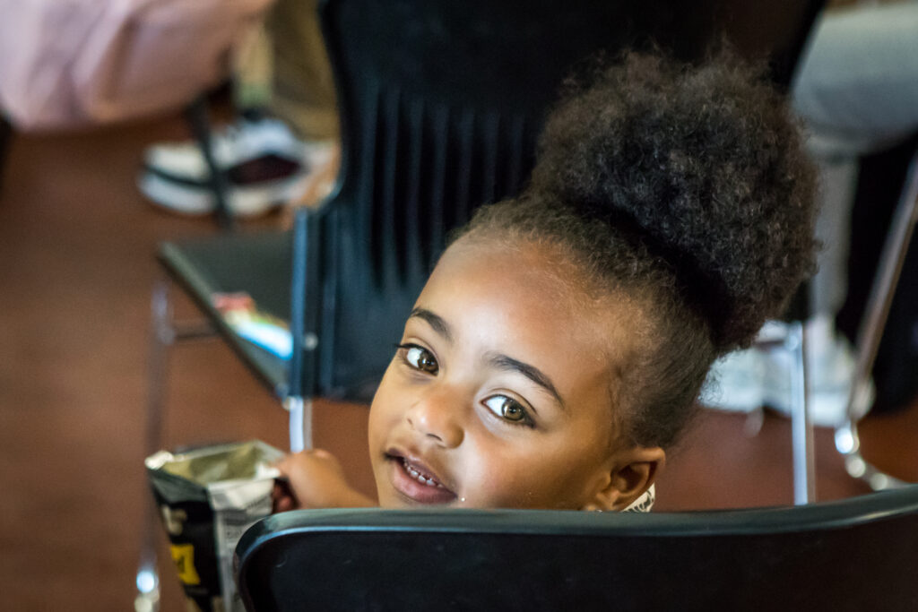 A little child with a poof of hair looks over their shoulder at the camera.