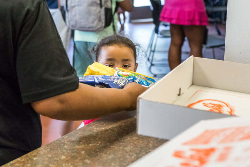 A little boy peeks over a countertop at boxes filled with hamburgers.