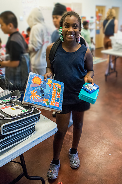 A young girl with beaded braids shows off new school supplies.
