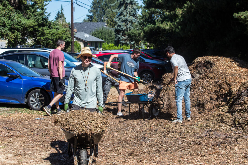 A group of volunteers shovel mulch from a giant pile into wheelbarrows and cart it away.
