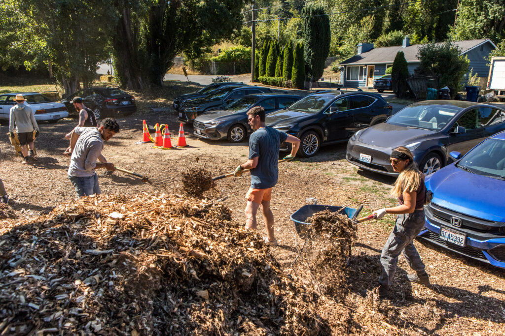 A group of volunteers shovel mulch from a giant pile into wheelbarrows and cart it away.