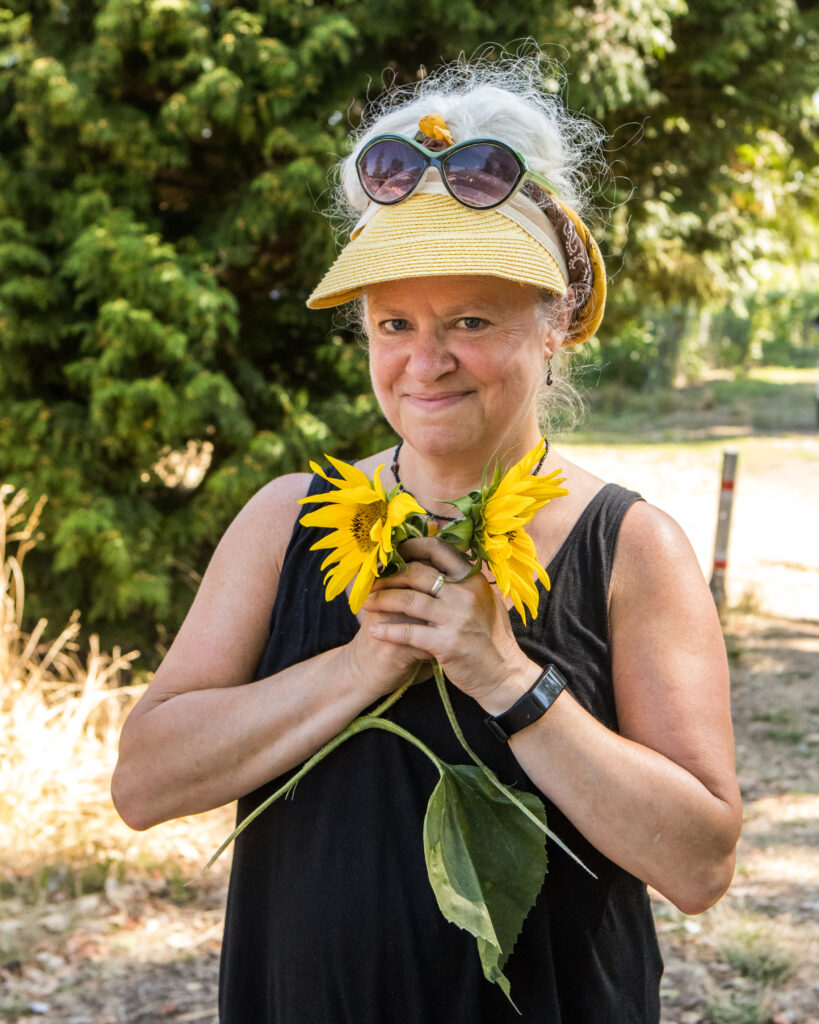 A woman in a yellow visor clutches a handful of sunflowers.