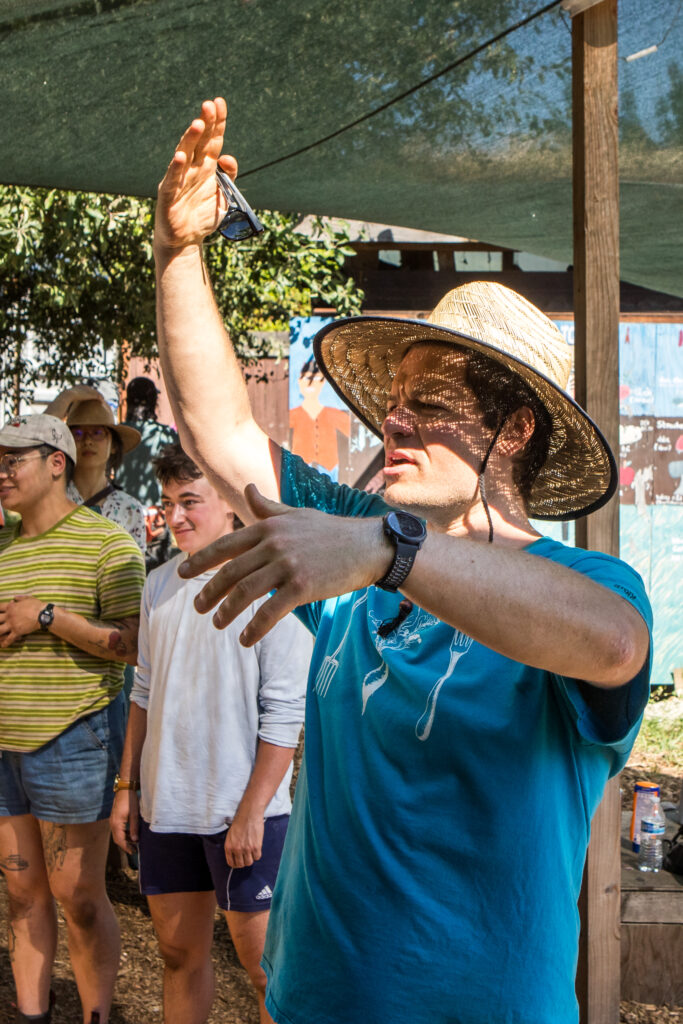 A man in a farmer's hat and blue shirt gestures as he speaks to a group.