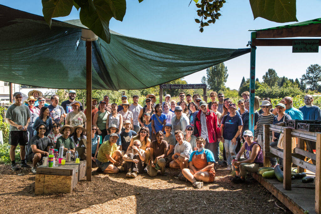 A crowd of people squeeze under a shade tarp for a group photo.