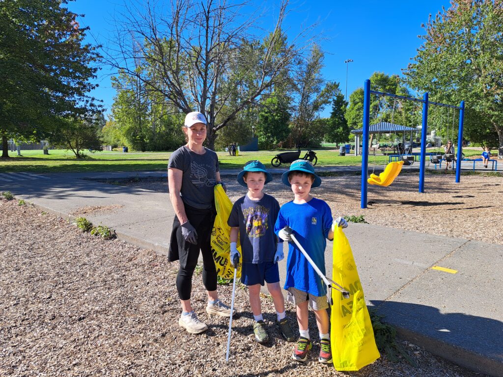 A mom and two kids pose while collecting trash in bright yellow trash bags.