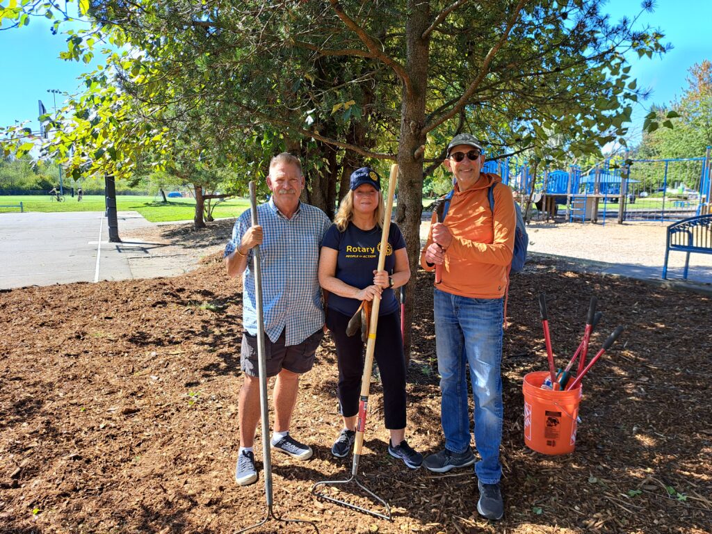 Three people pose under a tree surrounded by a fresh layer of mulch.