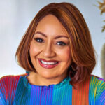 Headshot of a smiling woman with reddish-brown hair wearing a bright multi-colored top.