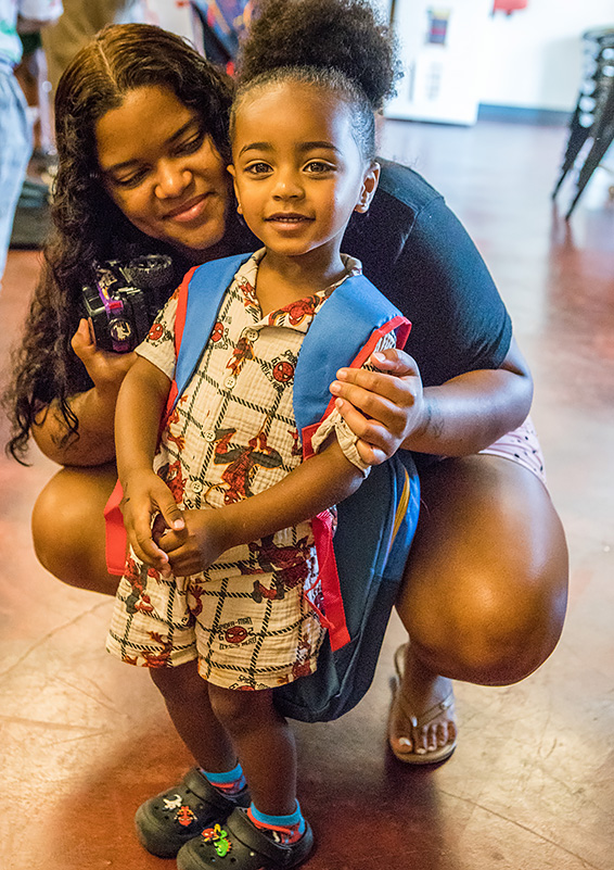 A mom crouches down by her little boy, who's wearing a Spider Man backpack.