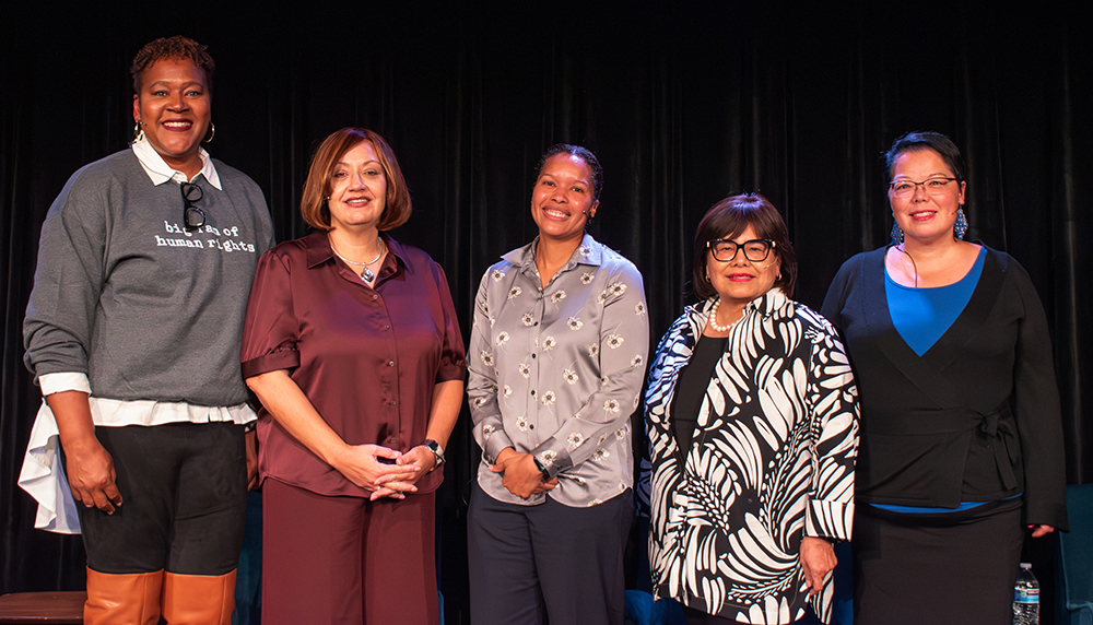 Five woman pose for a photo on a stage