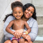 A smiling mother and son pose sitting on concrete steps