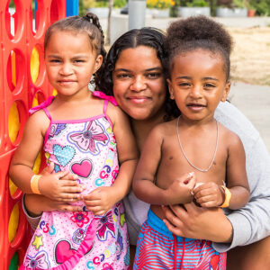 A woman crouches down to pose between a little girl on her left and a little boy on her right.