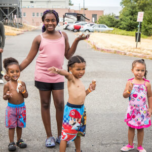 Three little kids and one tween, wearing summer clothes and bathing suits, eat ice cream cones.