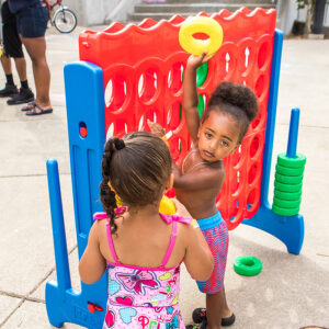 Two young kids in bathing suits play with a giant Connect Four game.