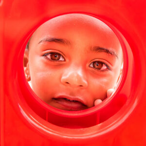 A little boy peeks through a circle in a red plastic game.