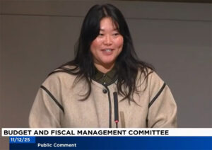 Screenshot of a woman with long dark hair testifying before a committee. The screen reads "Budget and fiscal management committee," "public comment," and 11/12/25."