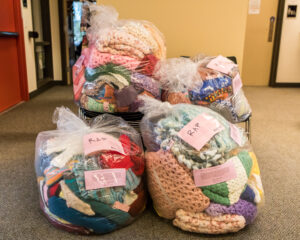 Clear plastic bags filled with knitted items, with pink slips of paper with writing on them inside.