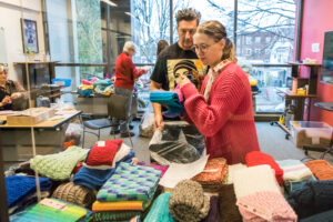 Several people sort and bag knitted hats, scarves, and gloves.