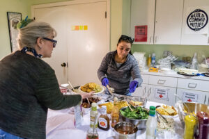 Two women leaning over a table piled high with food.
