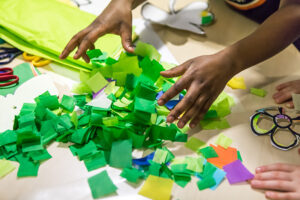 A child's hands tossing pieces of colorful crepe paper into a pile on a tan;e/