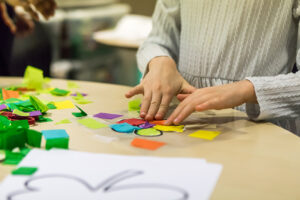A child's hands placing pieces of colorful paper into the shape of a flower blossom.
