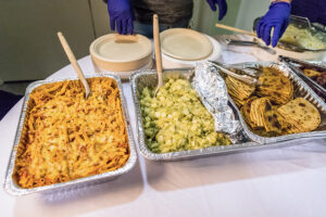 Metal trays full of rice, chicken drumsticks, casseroles, and other foods.