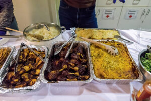 Metal trays full of rice, chicken drumsticks, casseroles, and other foods.