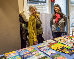 Two women smiling as they stand behind a table covered in picture books.