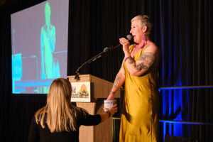 A women in a gold dress speaking into a microphone