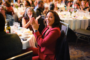 A women clapping while seated in a crowded ballroom