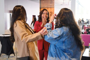 A women clasps her hands over her mouth while talking to two peole