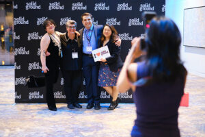 A photographer takes a picture of three people holding signs in front of a backdrop.