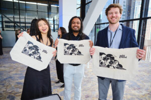 Three people holding screen-printed tote bags.