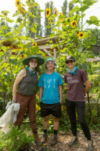 Three people posing infront of several tall sunflowers.