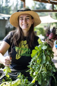 A volunteer in a straw hat holds up a bunch of freshly harvested beets.