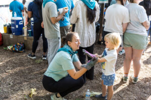 A woman helps a young boy put on a pair of gardening gloves.