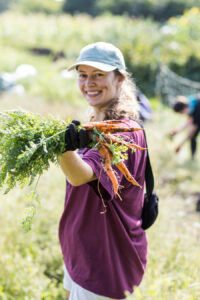 A woman holds up a bunch of freshly harvested carrots