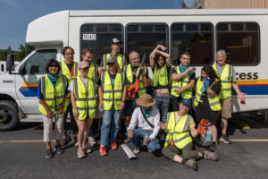 A group of volunteers, most of them in reflective vests, in front of a paratransit vehicle