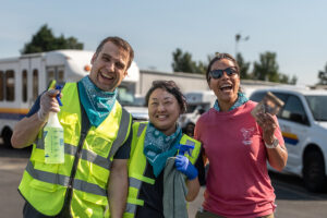 Two people in reflective vests and a woman in a salmon-colored shirt in a transit yard.