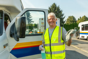 A volunteer in a reflective vest holding a wash rag in one hand while standing infront of the open door of a paratransit vehcile.