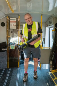 A volunteer in a reflective vest holding a leaf blower inside a para transit vehicle.