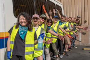 A row of volunteers in reflective vests with arms outstretched infront of a paratransit bus.