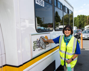 A volunteer in a reflective vest whipes down a a Solid Ground sign on the side of a paratransit bus.