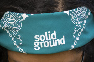 A close up of a teal Solid Ground bandana wrapped around someone's forehead.