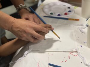 An adults hands clasped around the hands of a child holding a paint brush