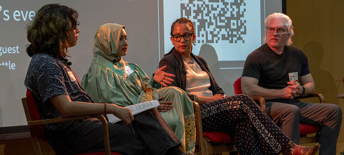 Four people of diverse ages and ethnicities sit on a stage, engaged in conversation.